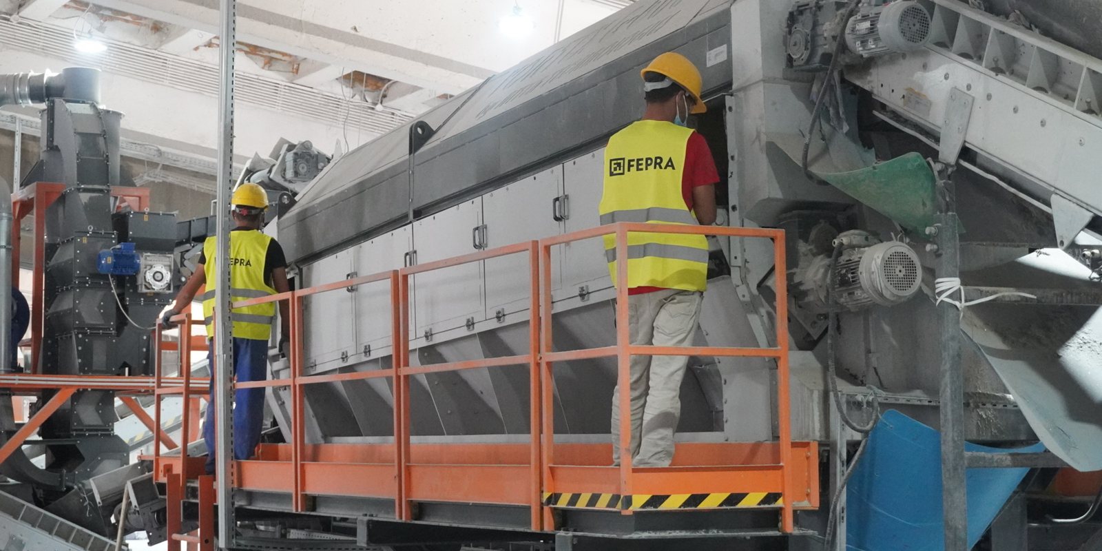 Two FEPRA colleagues in hi-vis vests on the walkway of the glass recycling line in Buftea