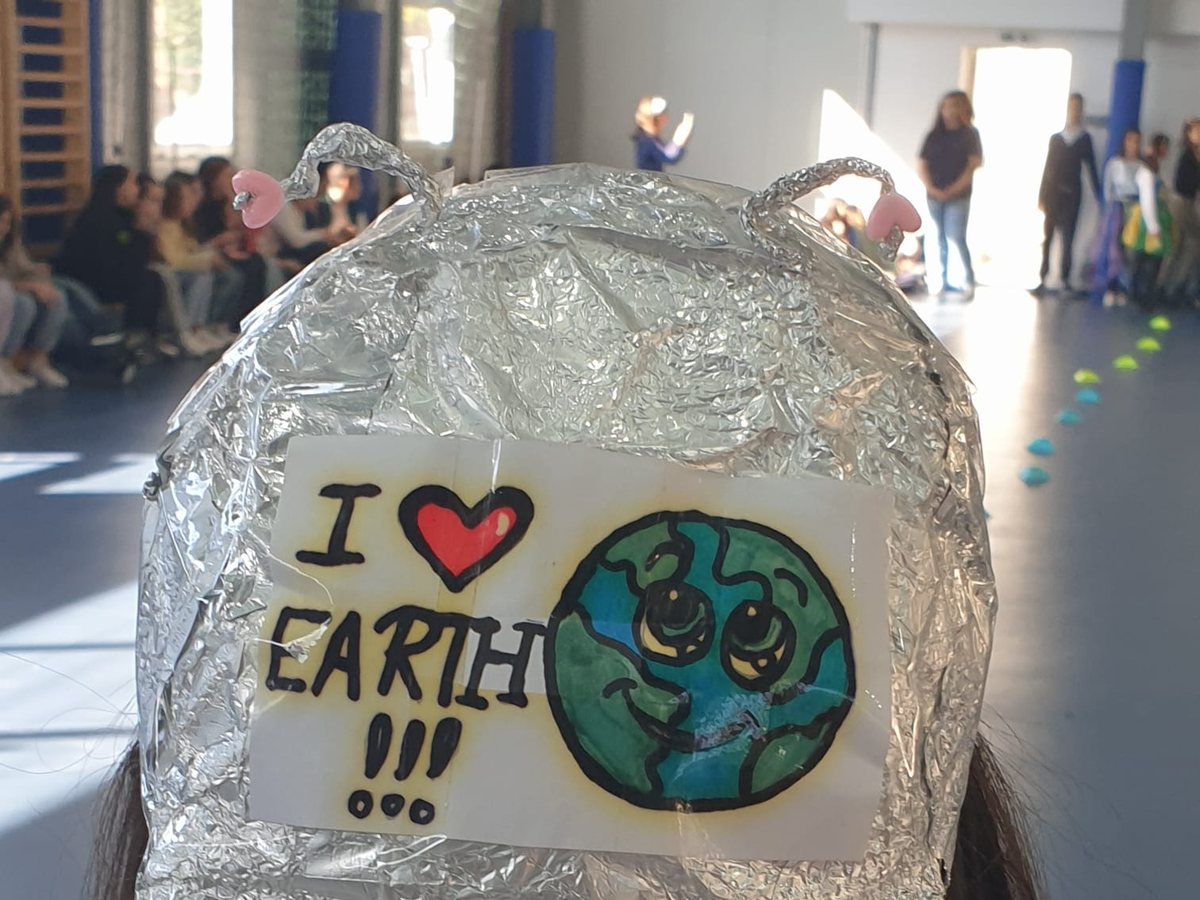 A child in a school gym wearing a foil cap that reads “I love Earth”, at an environmental-education workshop