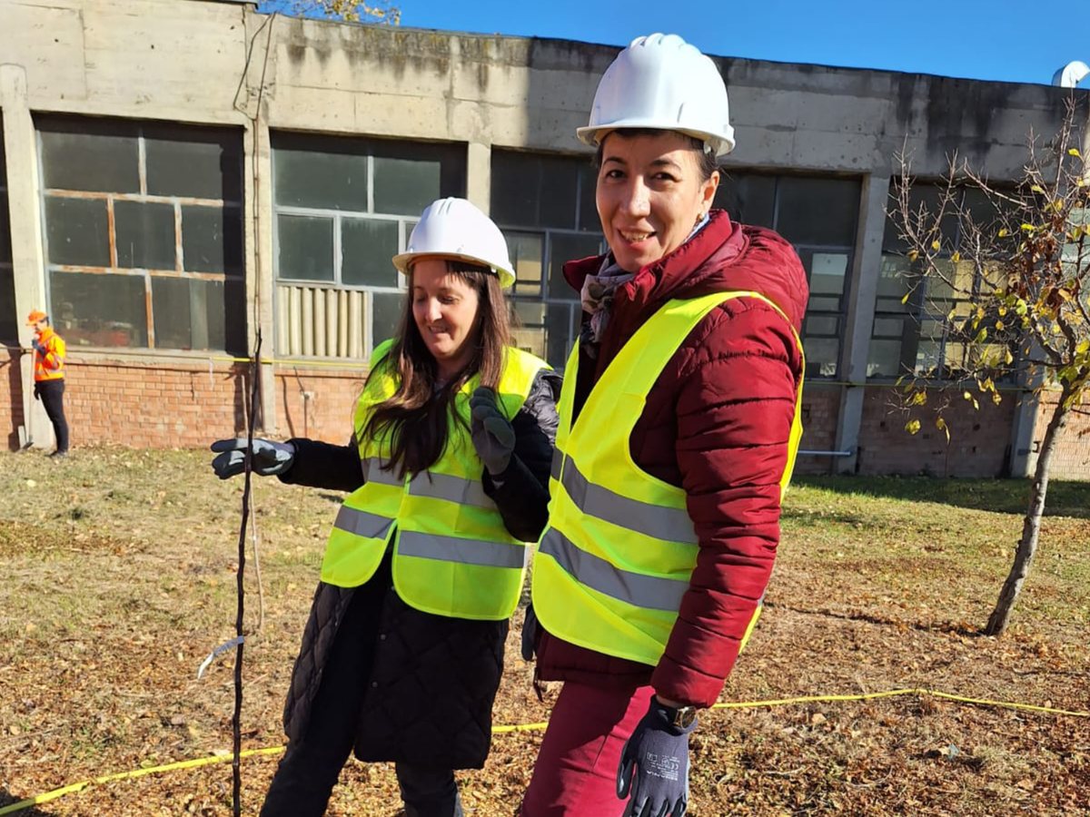 Two GIS colleagues, in hard hats, at a tree-planting action on an industrial site